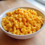 A close-up of rich, creamy Instant Pot Mac and Cheese served in a white bowl on a wooden surface.