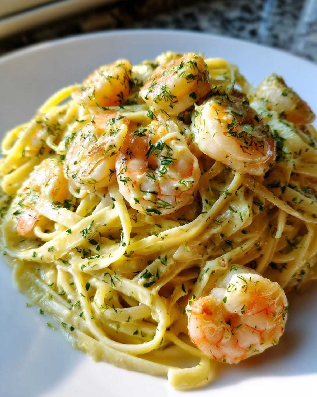 A close-up view of a serving of Creamy Lemon Garlic Shrimp Pasta, featuring fettuccine coated in a rich sauce and topped with seasoned shrimp.