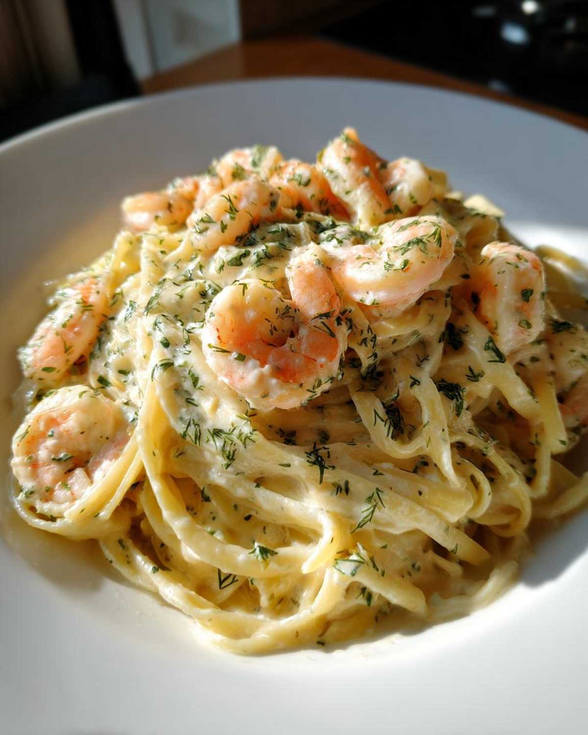 A close-up of rich Creamy Lemon Garlic Shrimp Pasta featuring fettuccine noodles coated in a white sauce and topped with pink shrimp and green herbs.