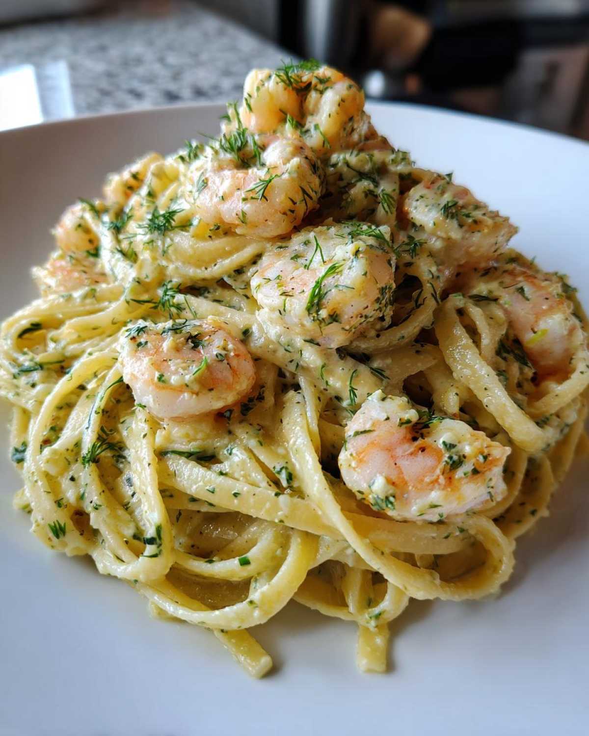 Close-up of a mound of Creamy Lemon Garlic Shrimp Pasta tossed in a rich sauce and topped with pink shrimp and fresh dill.
