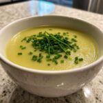 Close-up of a bowl of smooth, yellow Creamy Potato Leek Soup topped with fresh, chopped chives.