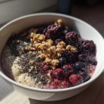 Close-up of a Creamy Vanilla Protein Smoothie Bowl topped with blackberries, blueberries, chia seeds, and granola.