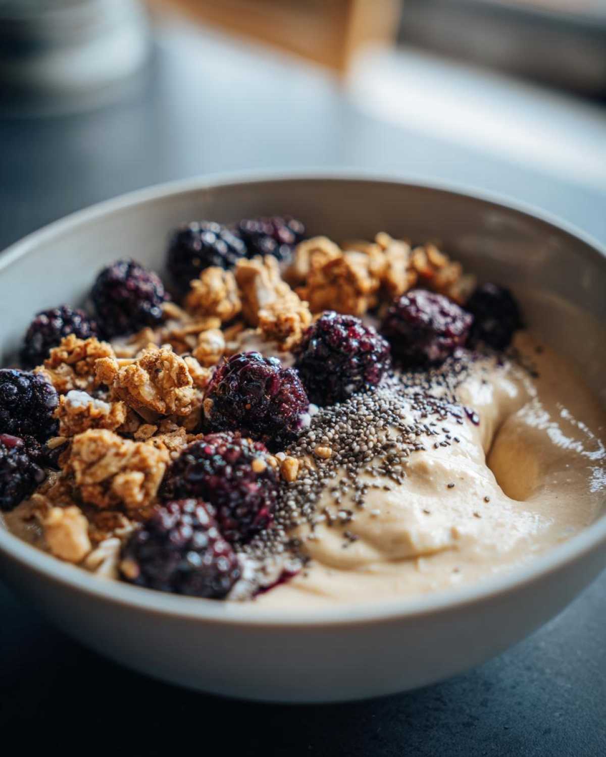 Close-up of a Creamy Vanilla Protein Smoothie Bowl topped with blackberries, granola, and chia seeds.