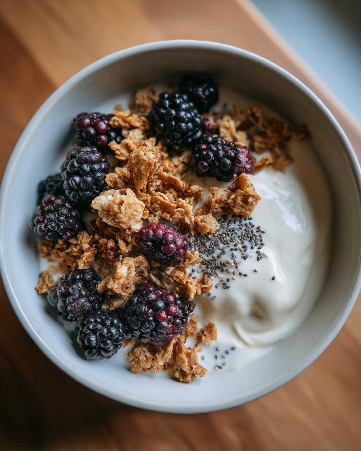 Close-up of a bowl topped with blackberries, granola, and chia seeds, representing a Creamy Vanilla Protein Smoothie Bowl.