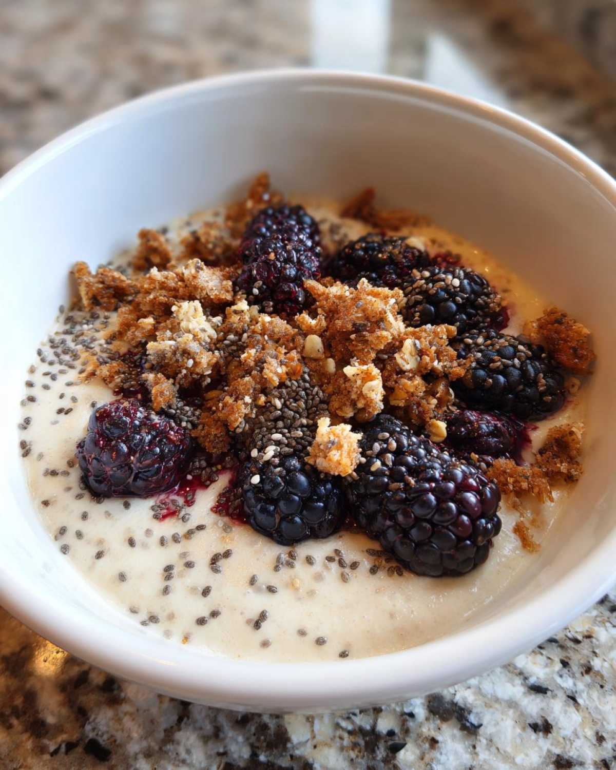Close-up of a Creamy Vanilla Protein Smoothie Bowl topped with blackberries, chia seeds, and granola.