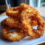 Close-up of golden brown, crispy Air Fryer Onion Rings piled on a white plate.