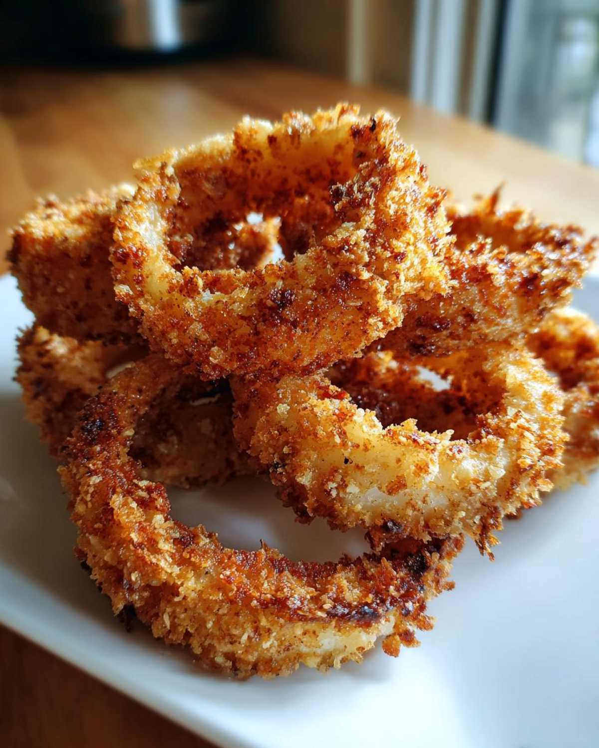 Close-up of several golden brown, crispy Air Fryer Onion Rings piled on a white plate.