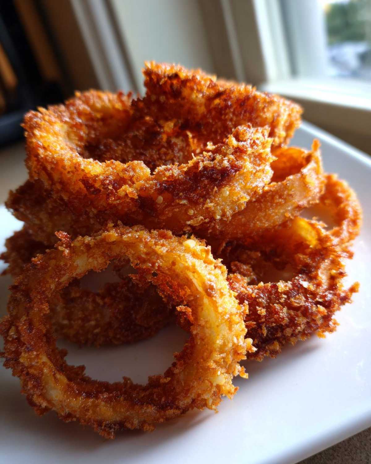Close-up of a stack of perfectly golden brown, crispy Air Fryer Onion Rings on a white plate.