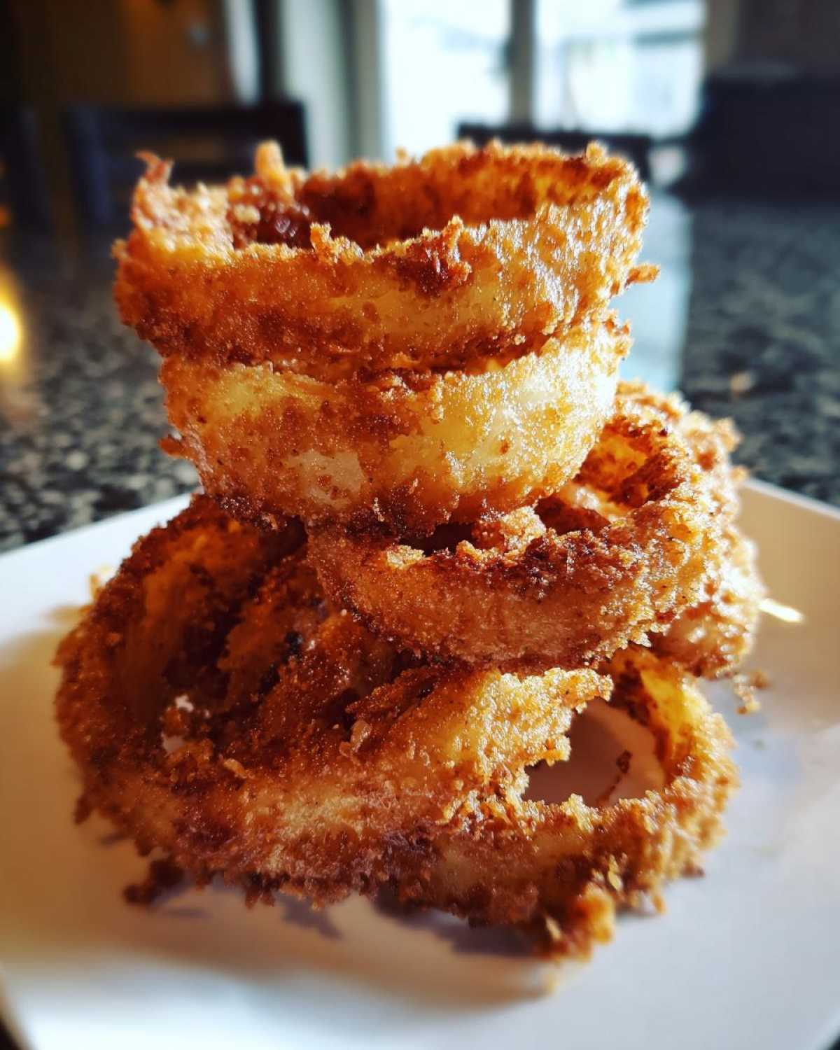 A close-up stack of golden brown, crispy Air Fryer Onion Rings served on a white plate.