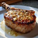 A close-up of a thick, bone-in Crispy Air Fryer Pork Chop topped with glistening garlic butter.