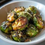 Close-up of perfectly roasted Crispy Parmesan Brussels Sprouts topped with grated cheese in a white bowl.