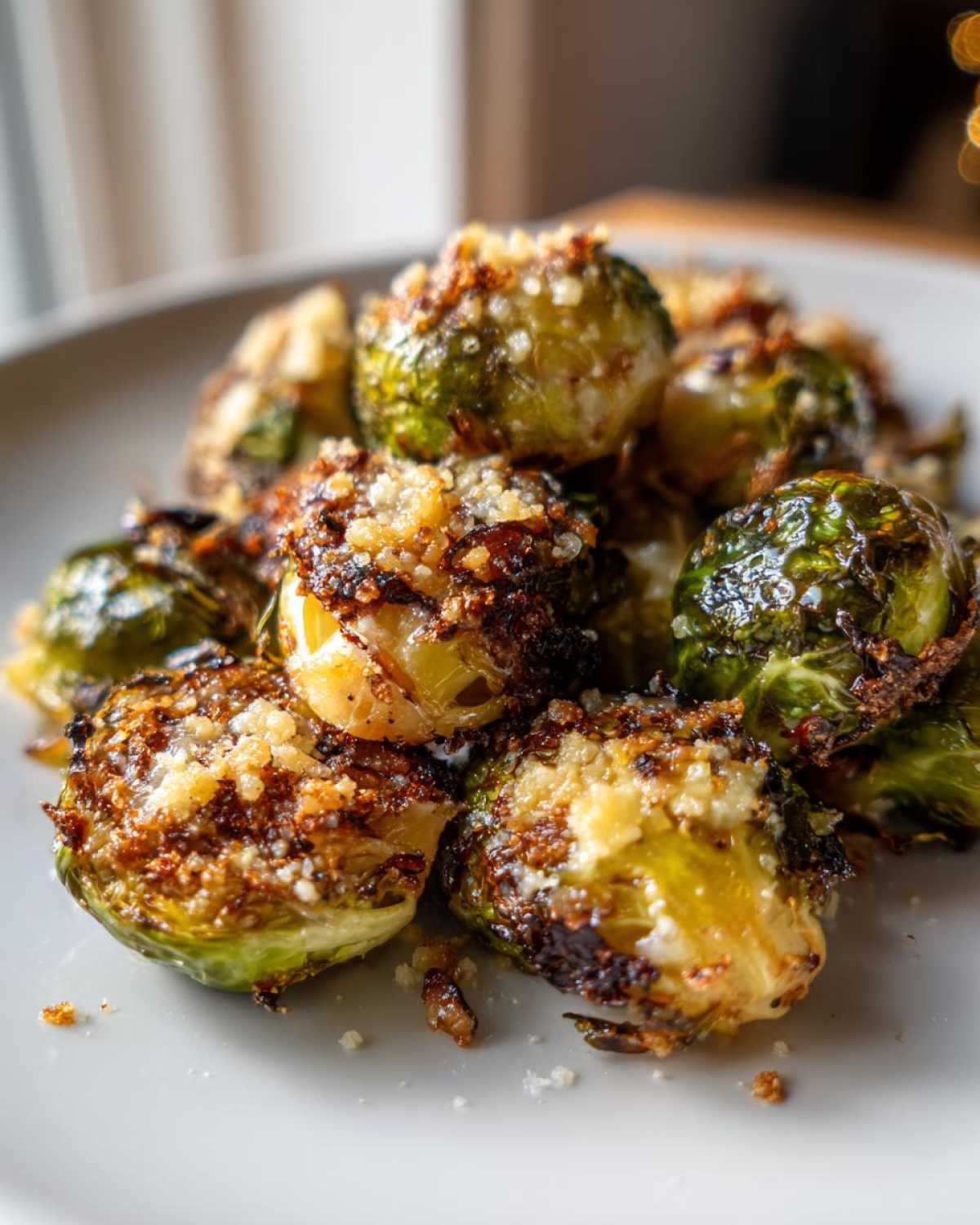 A close-up of perfectly roasted Crispy Parmesan Brussels Sprouts piled on a white plate.