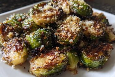 Close-up of perfectly roasted Crispy Parmesan Brussels Sprouts topped with grated cheese on a white serving dish.