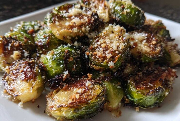 Close-up of perfectly roasted Crispy Parmesan Brussels Sprouts topped with grated cheese on a white serving dish.