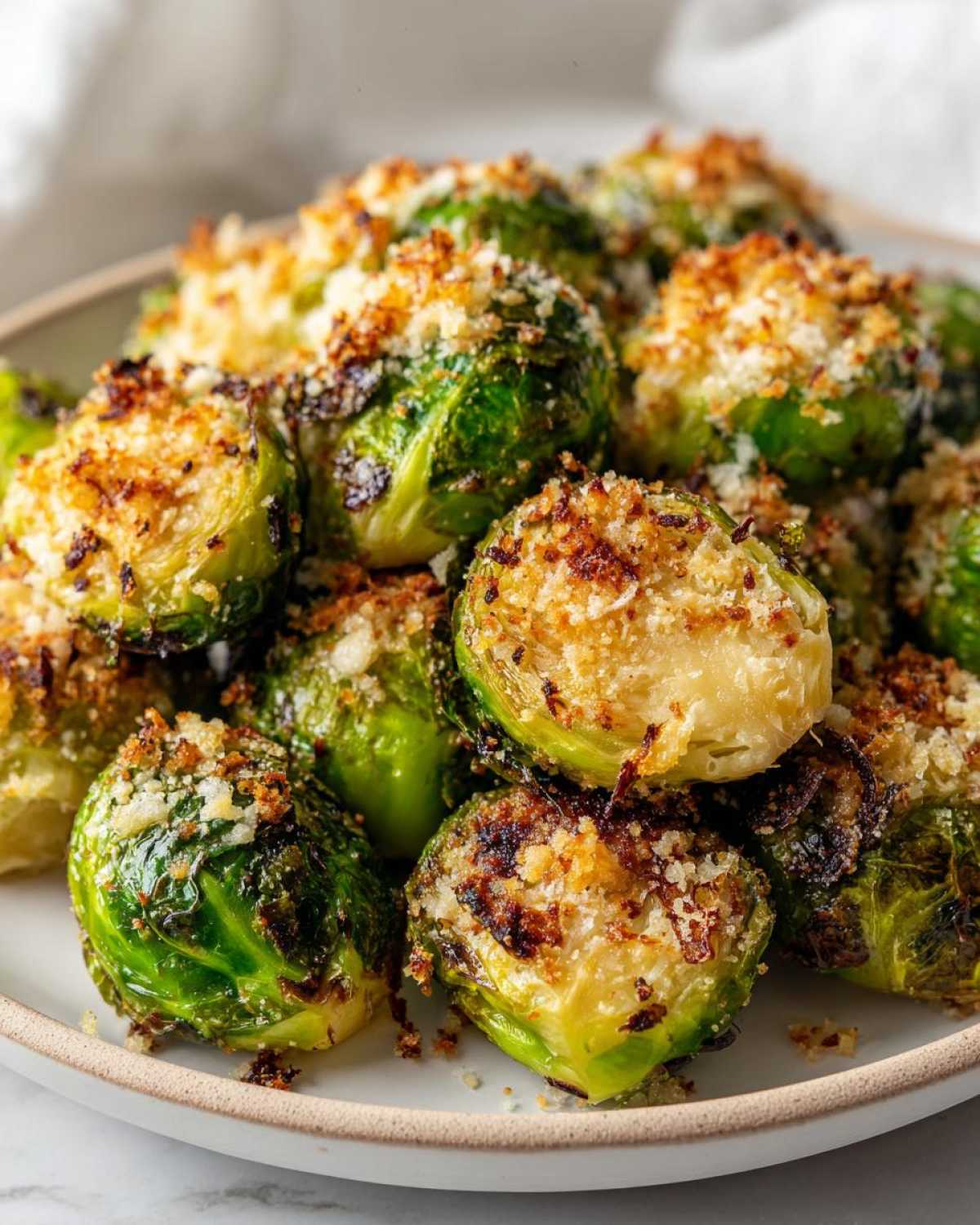 A close-up of roasted Crispy Parmesan Brussels Sprouts piled high on a light-colored plate.