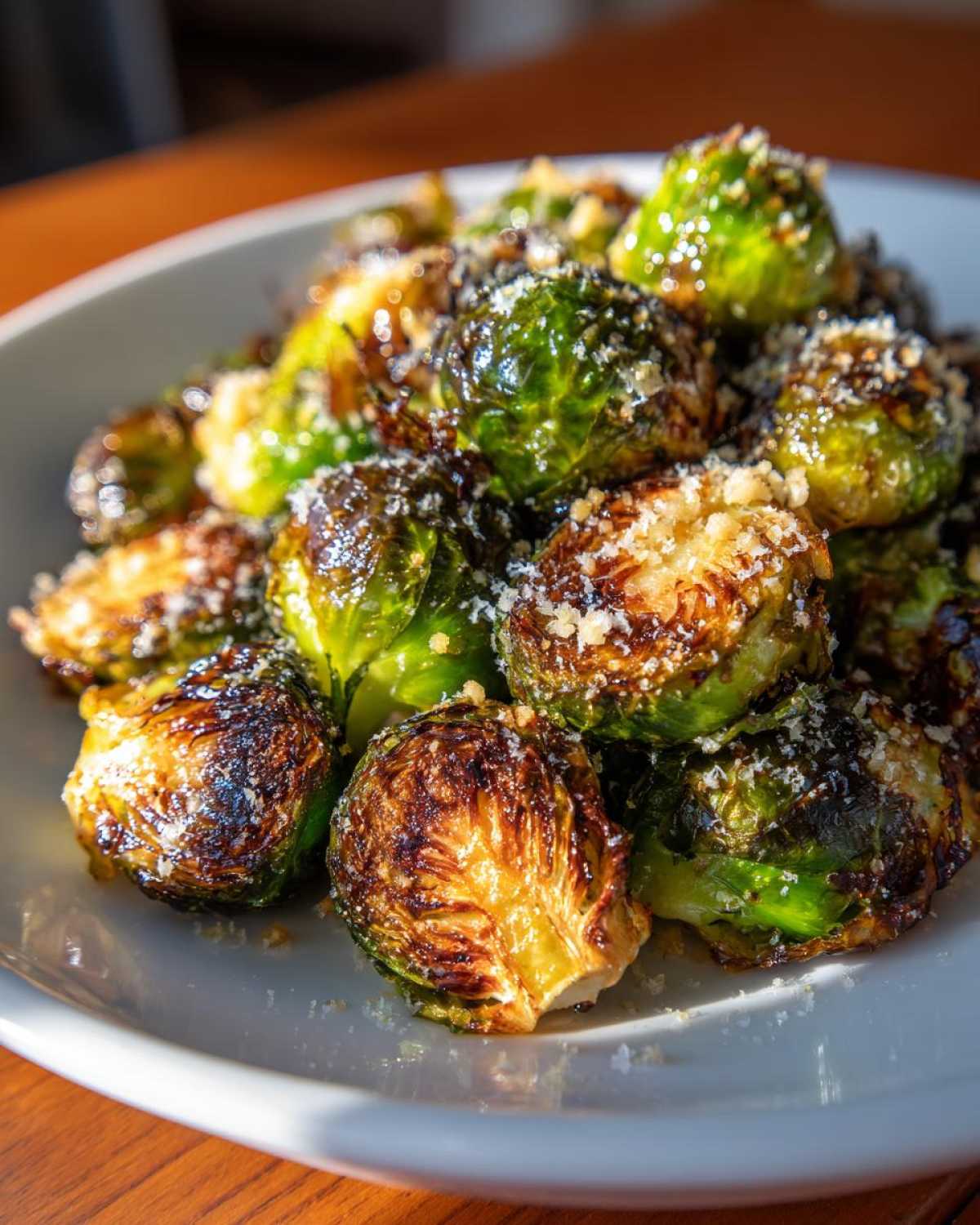 Close-up of roasted Crispy Parmesan Brussels Sprouts piled on a white plate, showing caramelized edges and grated cheese.
