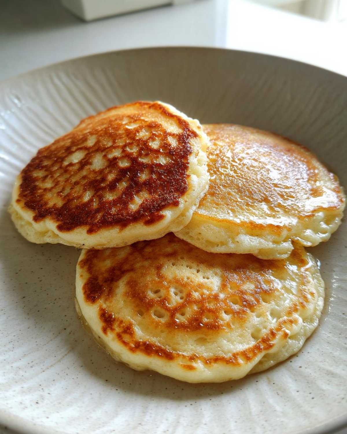 Three golden-brown Gluten-Free Buttermilk Pancakes stacked slightly on a speckled ceramic plate.