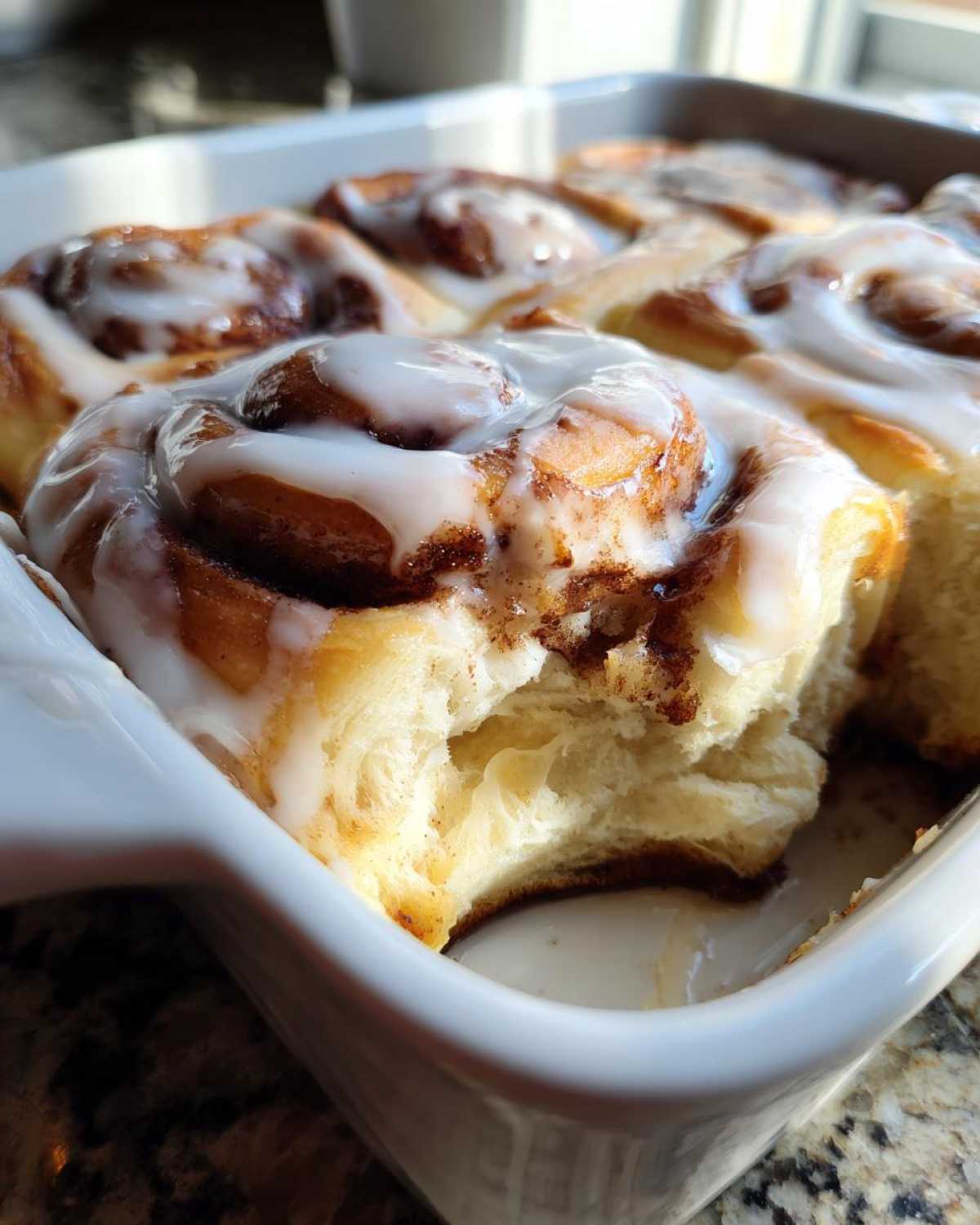 Close-up of fluffy Gluten-Free Cinnamon Rolls baked in a white dish, topped with thick white icing.