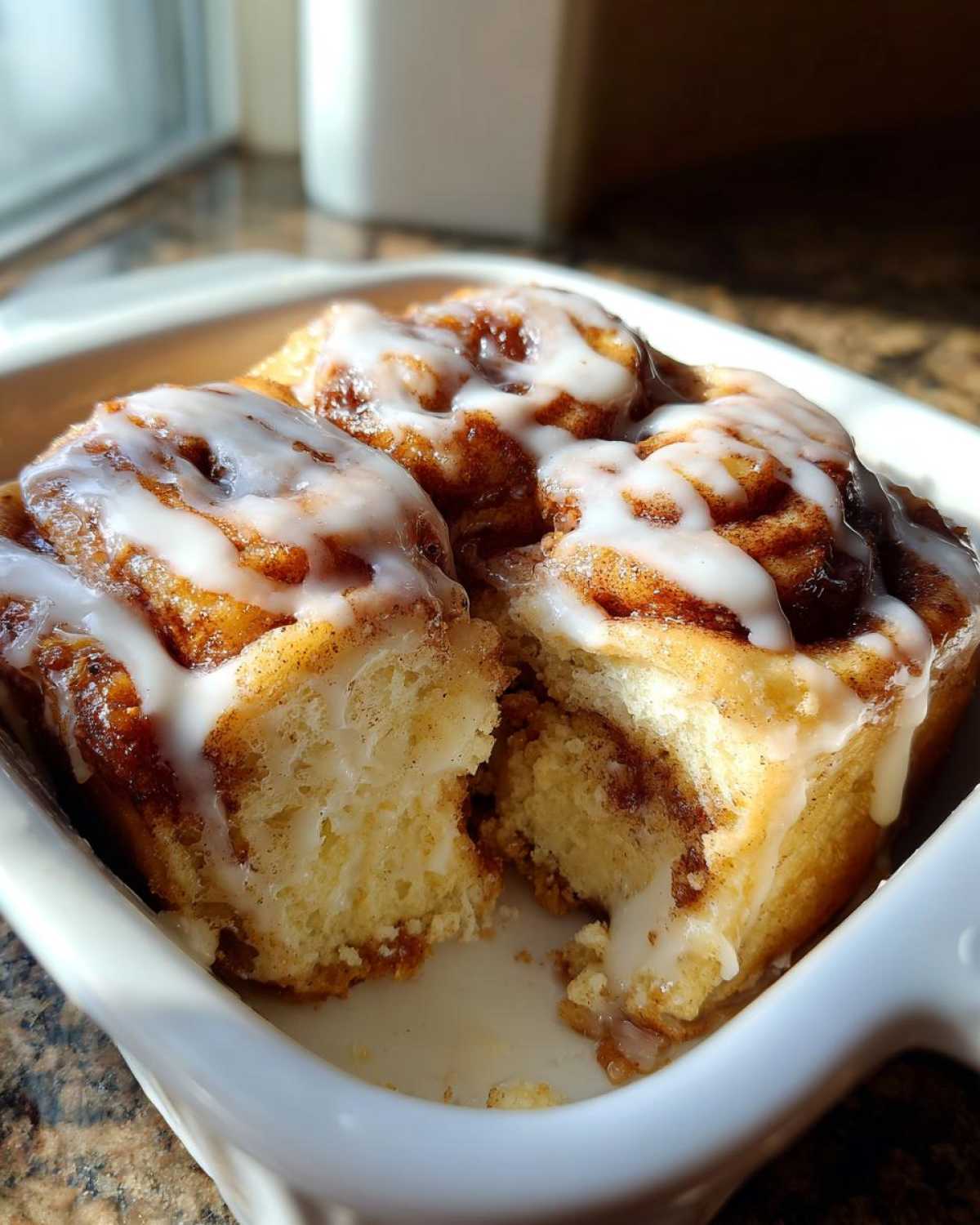 Close-up of three fluffy Gluten-Free Cinnamon Rolls topped with thick white icing in a white baking dish.
