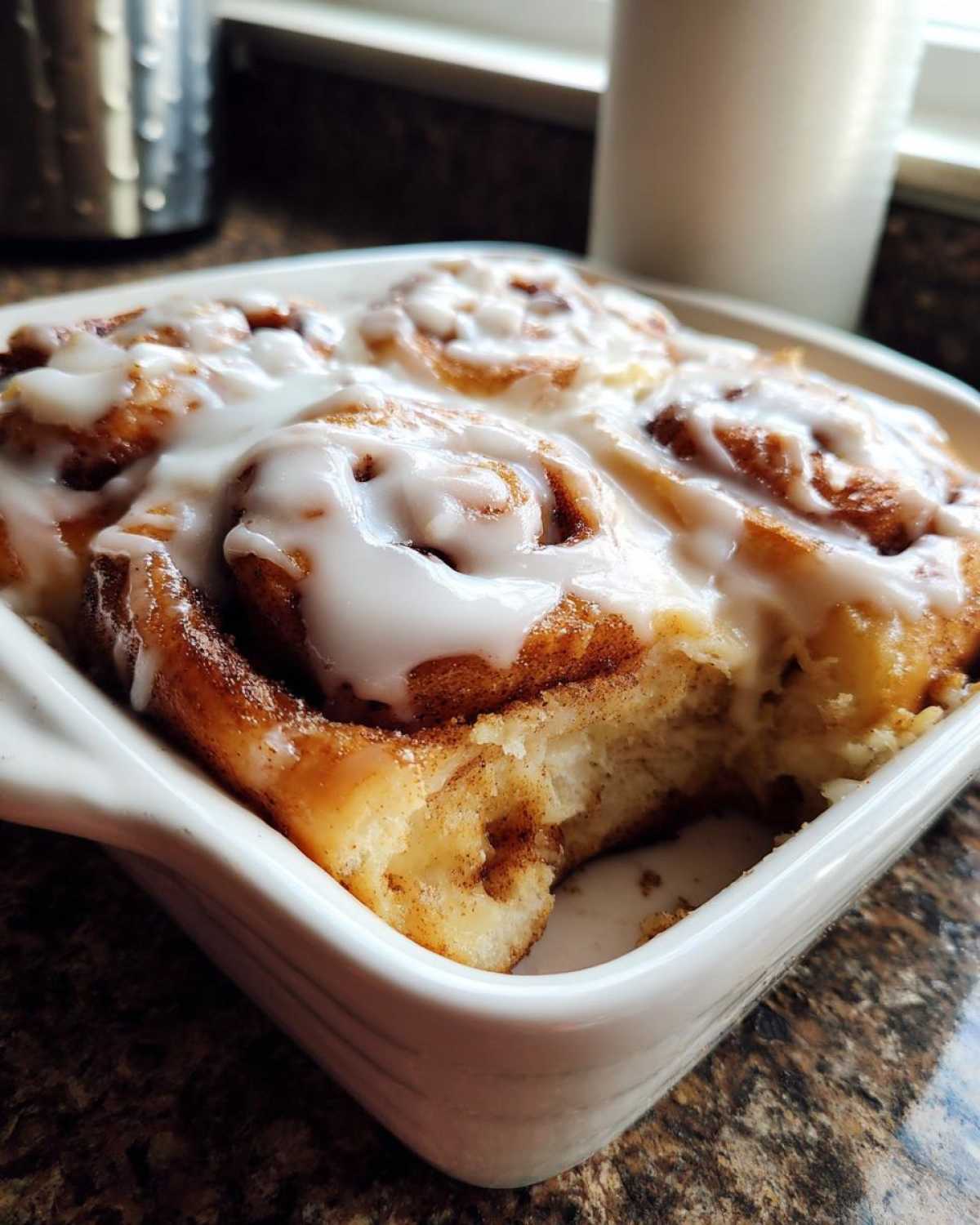 Close-up of fluffy Gluten-Free Cinnamon Rolls topped with thick white icing in a white baking dish.