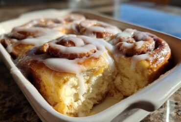 Close-up of freshly baked, fluffy Gluten-Free Cinnamon Rolls covered in white icing in a white baking dish.