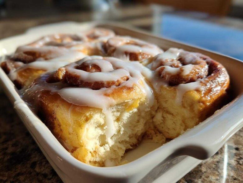 Close-up of freshly baked, fluffy Gluten-Free Cinnamon Rolls covered in white icing in a white baking dish.