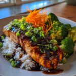 A close-up of a glazed salmon fillet served over white rice with broccoli and shredded carrots, part of Teriyaki Salmon Rice Bowls.