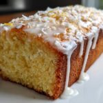 Close-up of a loaf of Gluten-Free Lemon Coconut Cake drizzled with white icing and topped with coconut flakes.