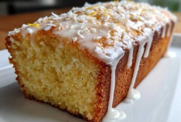 Close-up of a loaf of Gluten-Free Lemon Coconut Cake drizzled with white icing and topped with coconut flakes.