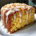 Close-up of a moist slice of Gluten-Free Lemon Coconut Cake topped with white glaze and toasted coconut flakes.