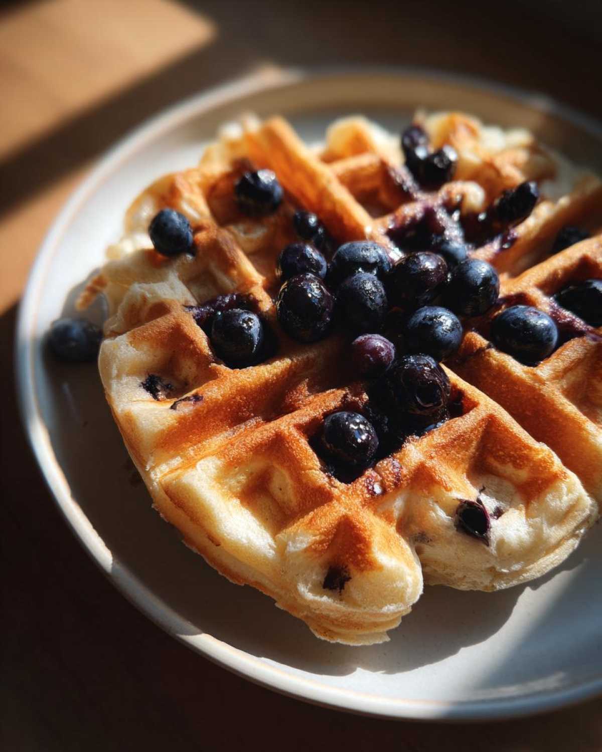 Close-up of golden Gluten-Free Blueberry Waffles topped generously with fresh blueberries and syrup.