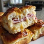 Close-up of a Hawaiian Roll Ham and Cheese Slider cut in half showing melted cheese pull.
