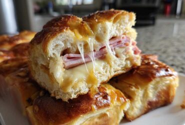 Close-up of a Hawaiian Roll Ham and Cheese Slider cut in half showing melted cheese pull.