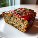 A close-up of a thick slice of Healthy Turkey Spinach Meatloaf topped with a bright red glaze and chives.
