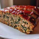 A thick slice of Healthy Turkey Spinach Meatloaf, showing the interior with ground turkey and green spinach, topped with a shiny red glaze.