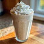 A tall glass filled with Homemade Vanilla Bean Frappuccino, topped high with whipped cream.
