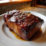 Close-up of a thick Honey Glazed Ham Steak in the Skillet, coated in a shiny, dark amber glaze with herbs.
