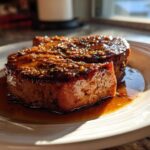 Close-up of two thick Honey Glazed Ham Steak in the Skillet portions resting in their sweet, brown glaze on a white plate.