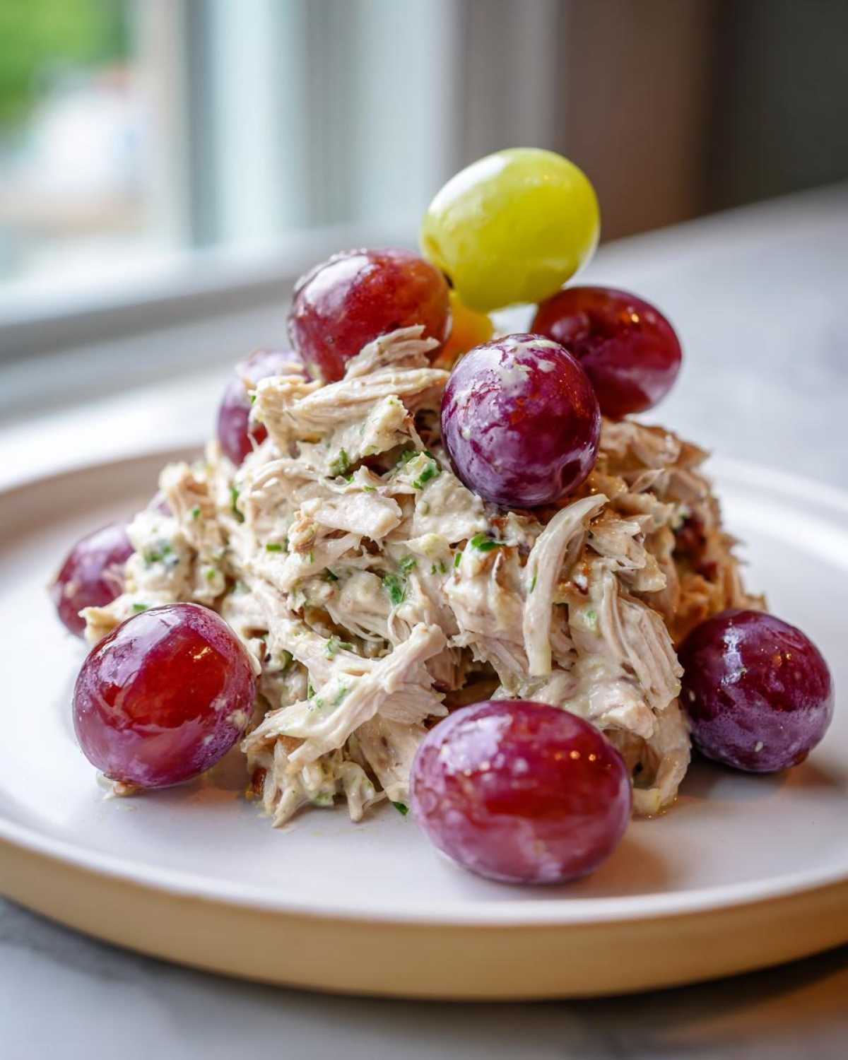 A mound of creamy Honey Mustard Chicken Salad with Grapes, garnished with whole red and green grapes on a white plate.