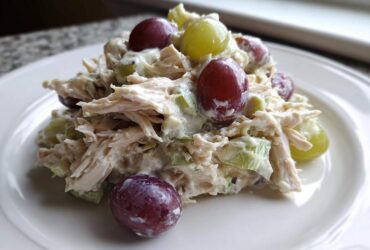 A close-up serving of creamy Honey Mustard Chicken Salad with Grapes and celery on a white plate.