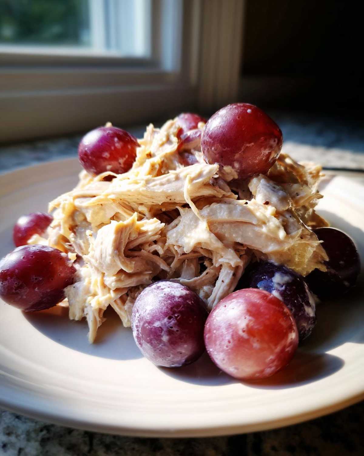 A serving of shredded Honey Mustard Chicken Salad with Grapes piled on a light plate.