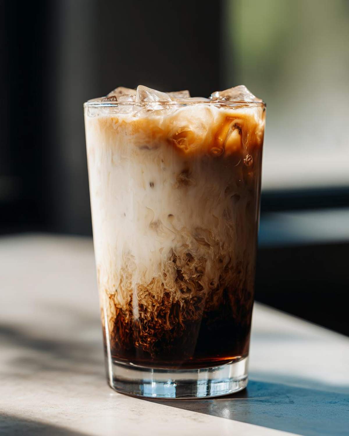 Close-up of a tall glass filled with an Iced Brown Sugar Oatmilk Latte showing rich brown syrup swirling into white oat milk and ice.