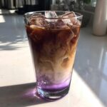 Close-up of an Iced Lavender Latte showing purple syrup, swirling cream, and dark coffee over ice cubes.