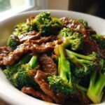 A close-up shot of glossy Instant Pot Beef and Broccoli served in a white bowl, featuring tender beef slices and bright green broccoli florets.