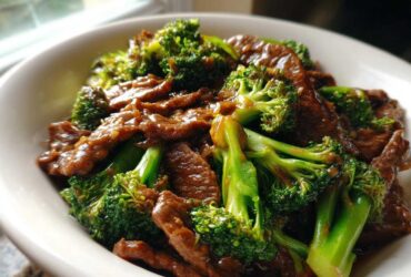A close-up shot of glossy Instant Pot Beef and Broccoli served in a white bowl, featuring tender beef slices and bright green broccoli florets.