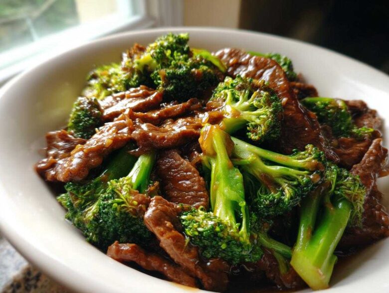 A close-up shot of glossy Instant Pot Beef and Broccoli served in a white bowl, featuring tender beef slices and bright green broccoli florets.