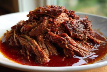 Close-up of shredded, saucy Instant Pot Beef Barbacoa piled high on a white plate, ready for tacos.