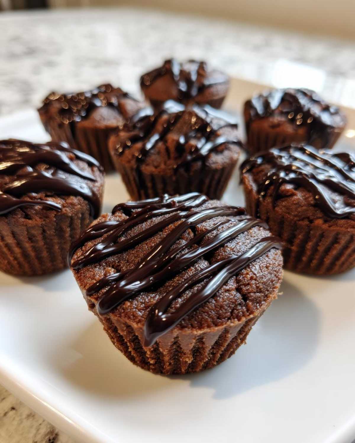 Several rich, dark chocolate Keto Chocolate Peanut Butter Fat Bombs drizzled with melted chocolate on a white plate.