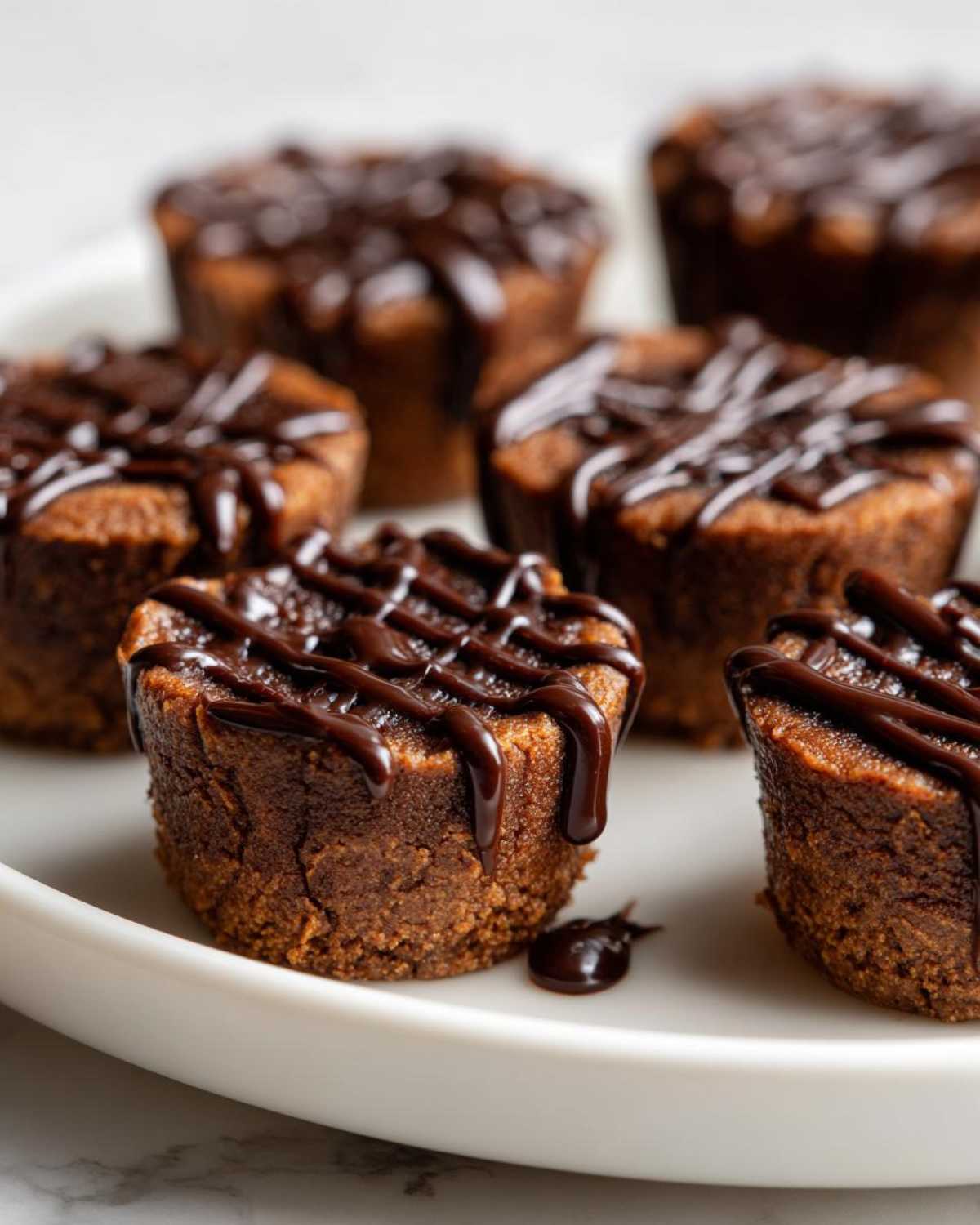 Several rich, dense Keto Chocolate Peanut Butter Fat Bombs drizzled with melted dark chocolate on a white plate.