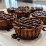 Close-up of several Keto Chocolate Peanut Butter Fat Bombs drizzled with chocolate sauce on a white platter.